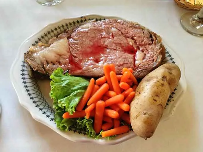 A thick slice of prime rib with a baked potato and carrots